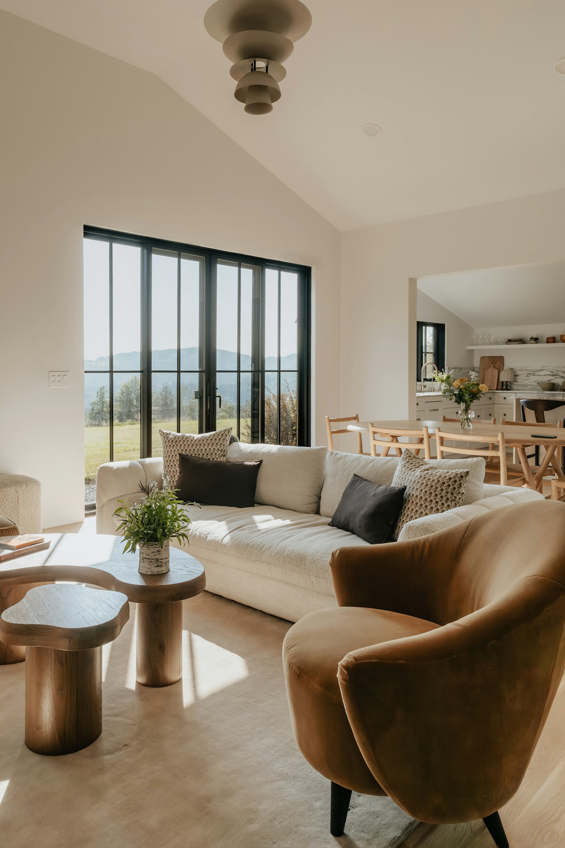 A sunlit living room with an ivory sofa, sculptural wooden tables and a taupe armchair